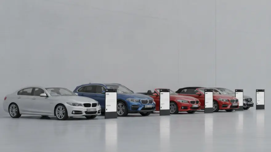 Een rij van verschillende auto's in diverse kleuren opgesteld in een lichte, minimalistische showroom met informatieborden ernaast.