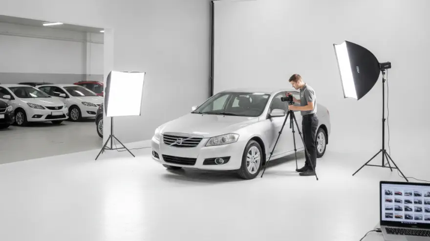 Un photographe prend en photo une voiture grise dans un studio de photographie automobile équipé de projecteurs.