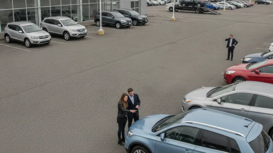 Ein Mann und eine Frau stehen auf dem Parkplatz eines Autohauses und betrachten ein hellblaues Auto.